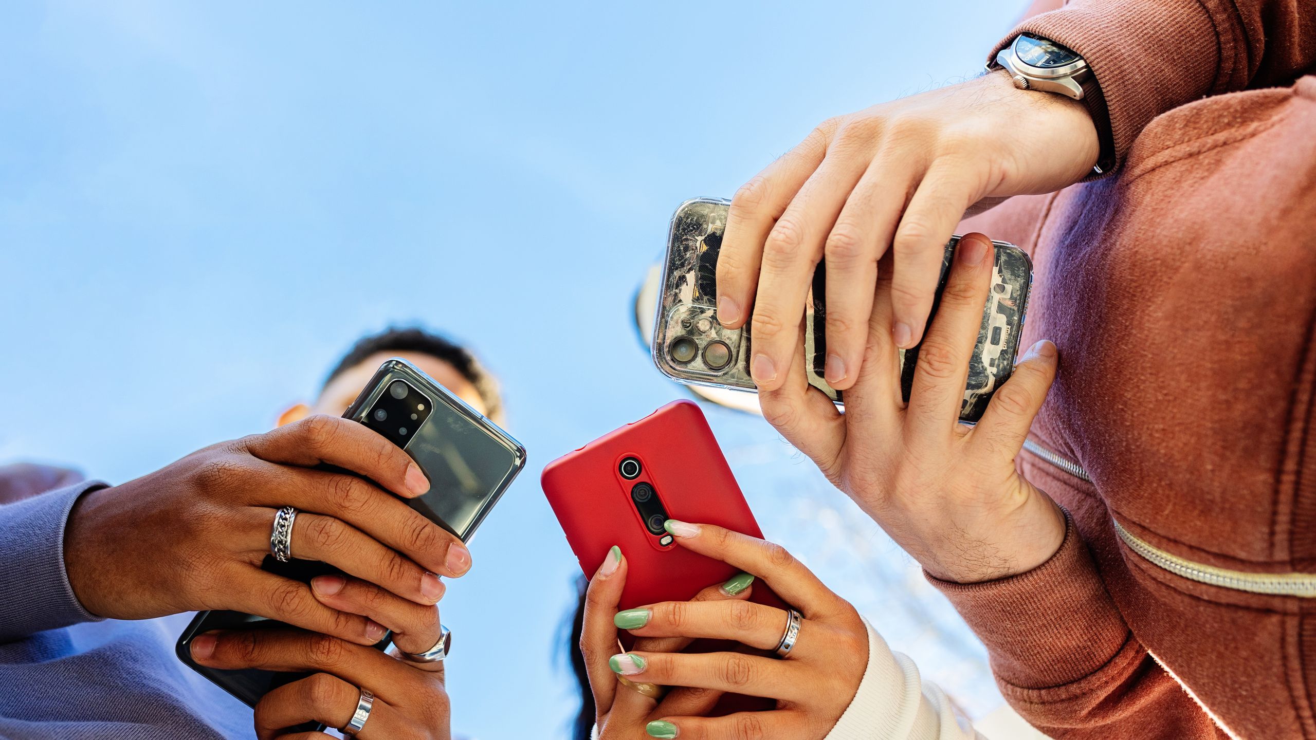 Low angle view of three young people using mobile phones outdoors.