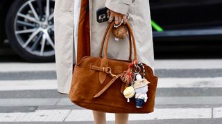 A guest wears red jumper white skirt beige long jacket brown suede Miu Miu aventure bag  with aLabubu charm white red...