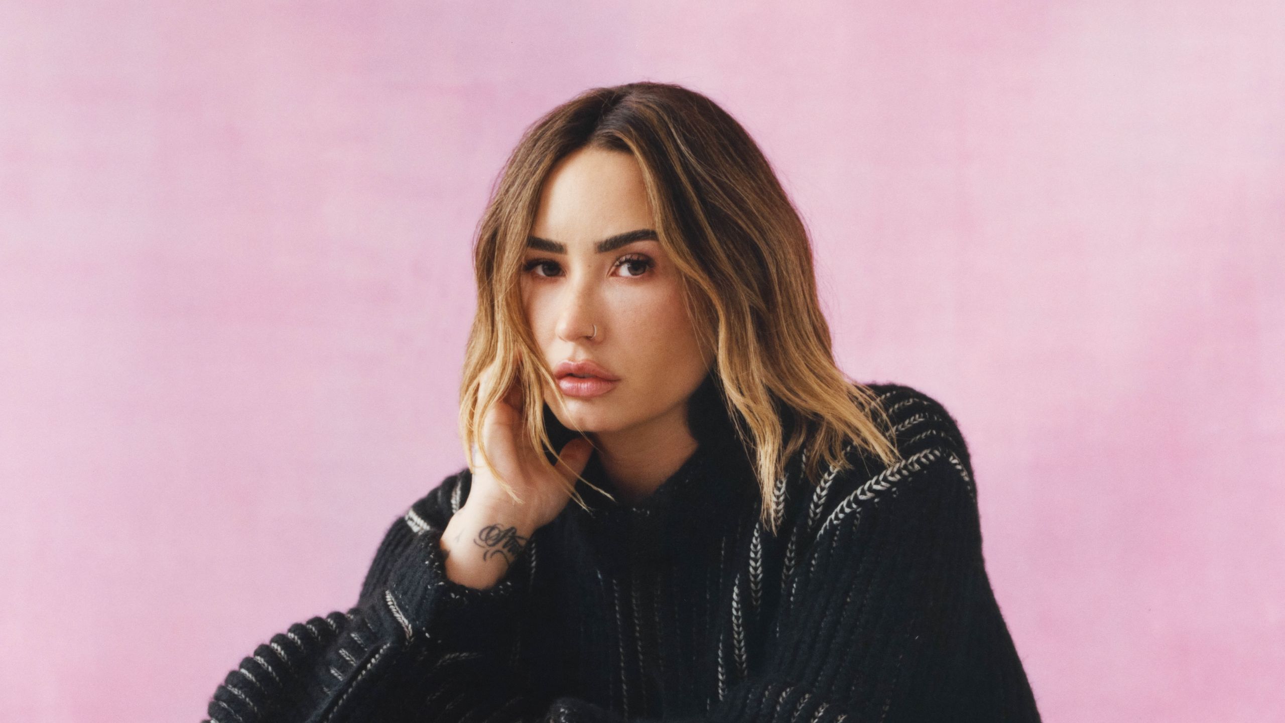 Demi against a marbled pink backdrop wearing an oversized black knit sweater.
